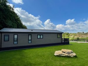 Modern holiday lodge with private decking on a well-maintained lawn at Saxon Park Lodges in Scarborough, set against a backdrop of trees and blue sky – ideal for year-round holiday home ownership
